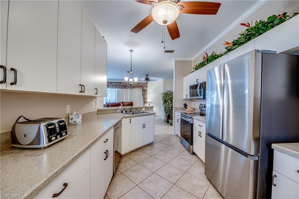 Kitchen with stainless steel appliances, white cabinetry, ornamental molding, hanging light fixtures, and a ceiling fan