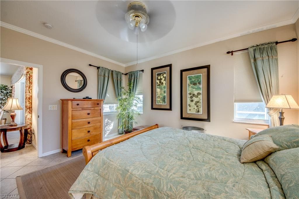 Tiled bedroom with crown molding, a ceiling fan, and multiple windows