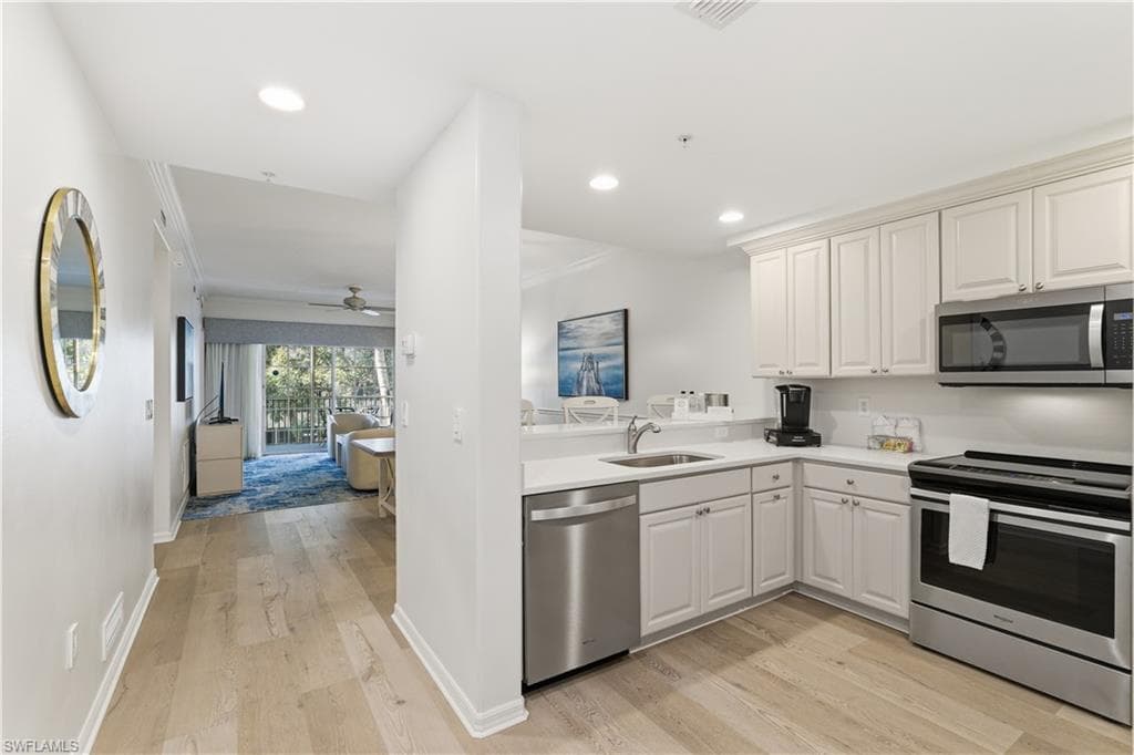 Kitchen featuring appliances with stainless steel finishes, light wood-type flooring, a ceiling fan, open floor plan, and ornamental molding