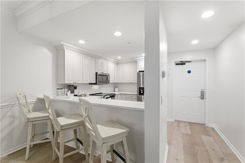 Kitchen featuring light wood-type flooring, a kitchen breakfast bar, white cabinets, recessed lighting, and stainless steel appliances