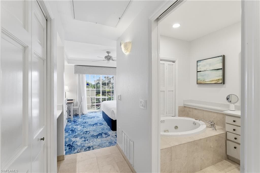 Ensuite bathroom featuring a closet, a ceiling fan, light tile patterned flooring, a jetted tub, and vanity