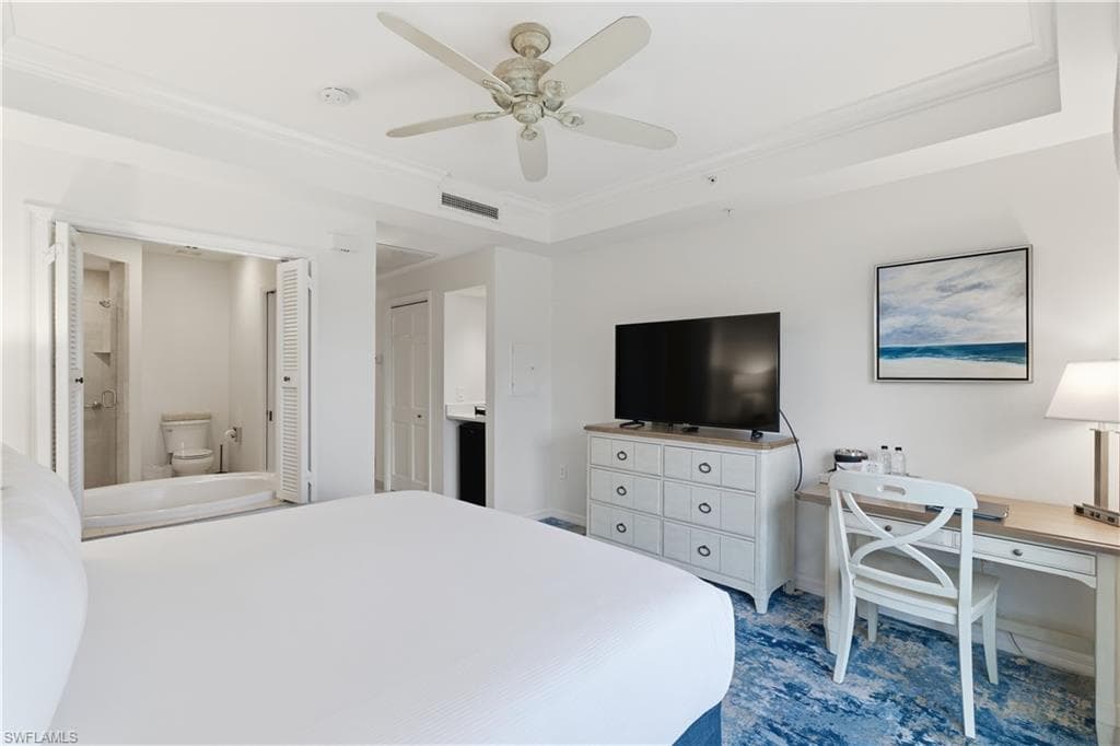 Bedroom featuring ensuite bathroom, ornamental molding, a desk, ceiling fan, and a tray ceiling