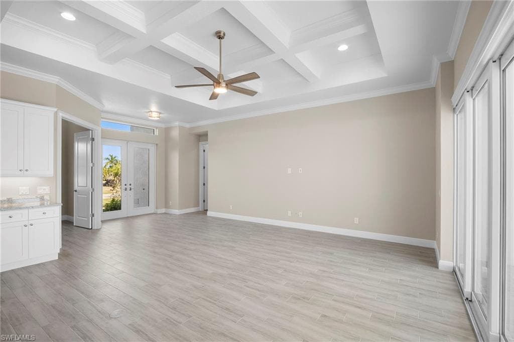 Unfurnished living room with coffered ceiling, beamed ceiling, crown molding, ceiling fan, and light wood-style flooring