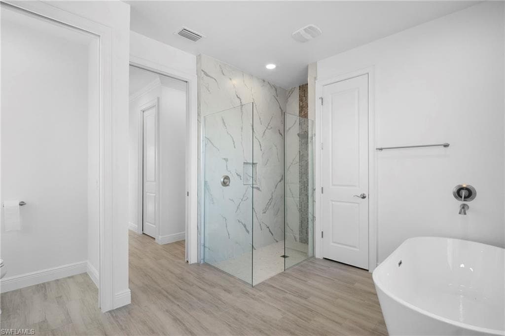 Full bath featuring a freestanding bath, a marble finish shower, light wood-type flooring, and recessed lighting