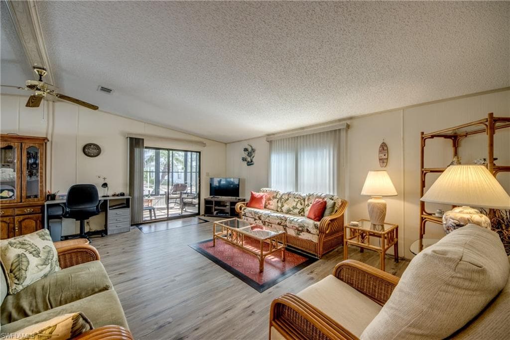 Living room featuring lofted ceiling, wood finished floors, a textured ceiling, a ceiling fan, and a desk