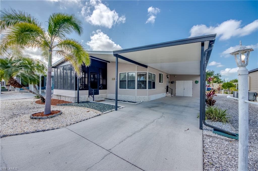 View of front of home featuring a sunroom, a carport, concrete driveway, and a patio
