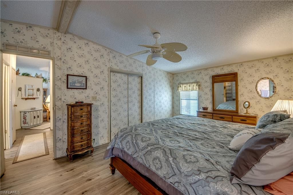 Bedroom featuring wood finished floors, a textured ceiling, ceiling fan, a closet, and wallpapered walls
