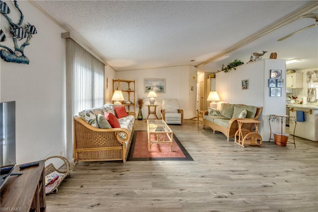 Living area featuring light wood finished floors, a textured ceiling, lofted ceiling, and a ceiling fan
