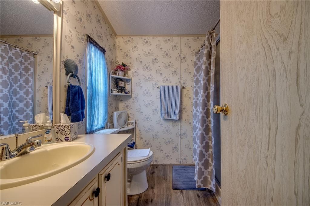 Bathroom featuring a shower stall, a textured ceiling, dark wood-type flooring, vanity, and wallpapered walls