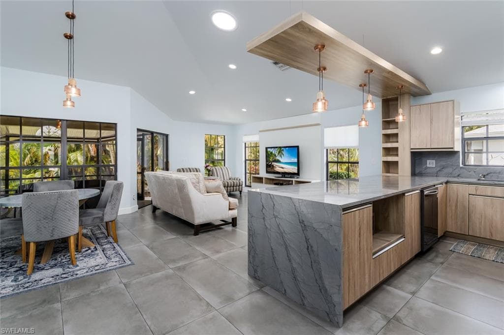 Kitchen featuring modern cabinets, dark stone counters, decorative backsplash, open floor plan, and light wood finish cabinets