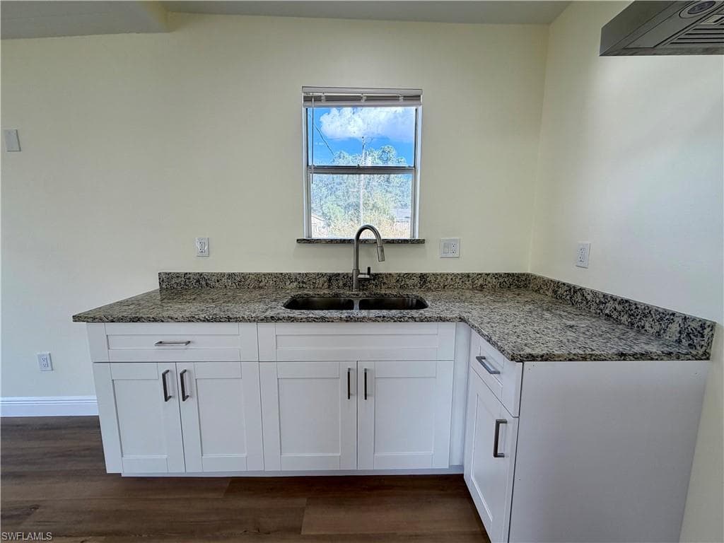 Kitchen with white cabinets, dark stone counters, exhaust hood, and dark wood finished floors