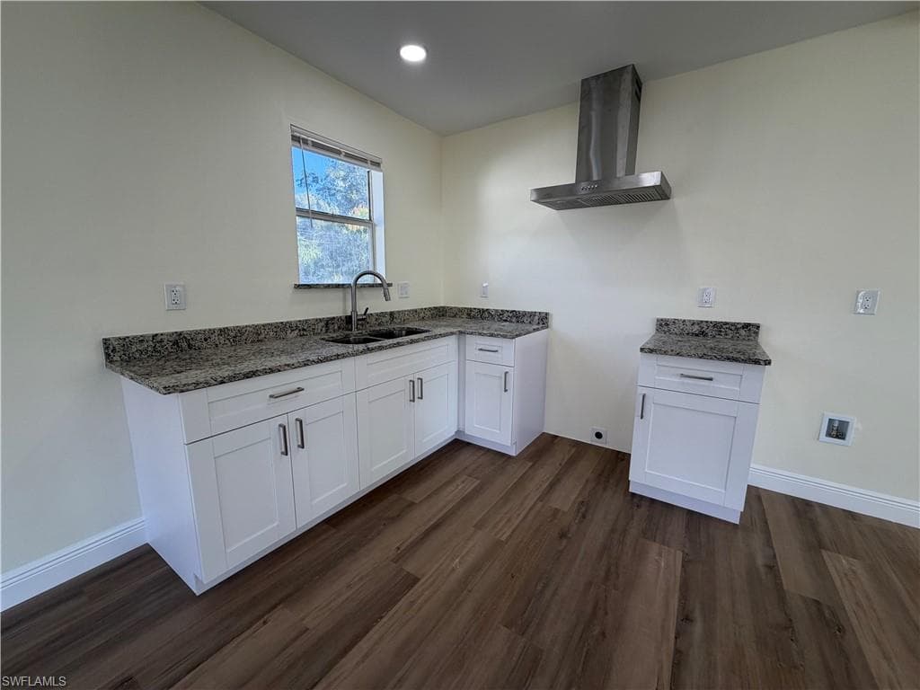 Kitchen with wall chimney exhaust hood, white cabinetry, dark stone countertops, dark wood-style flooring, and recessed lighting