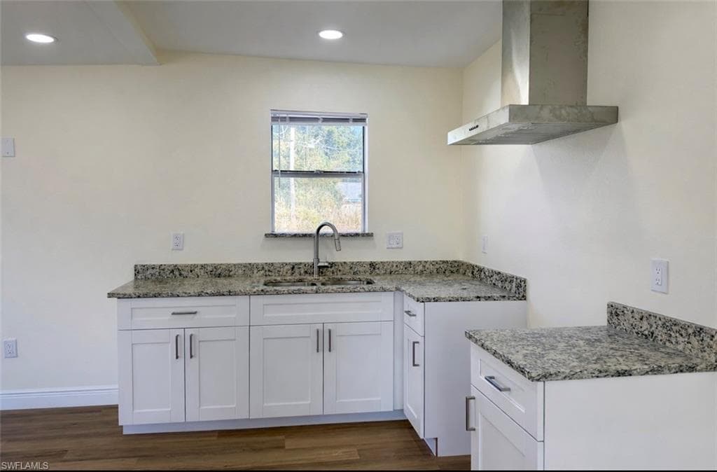 Kitchen featuring wall chimney range hood, white cabinets, light stone counters, dark wood-style floors, and recessed lighting