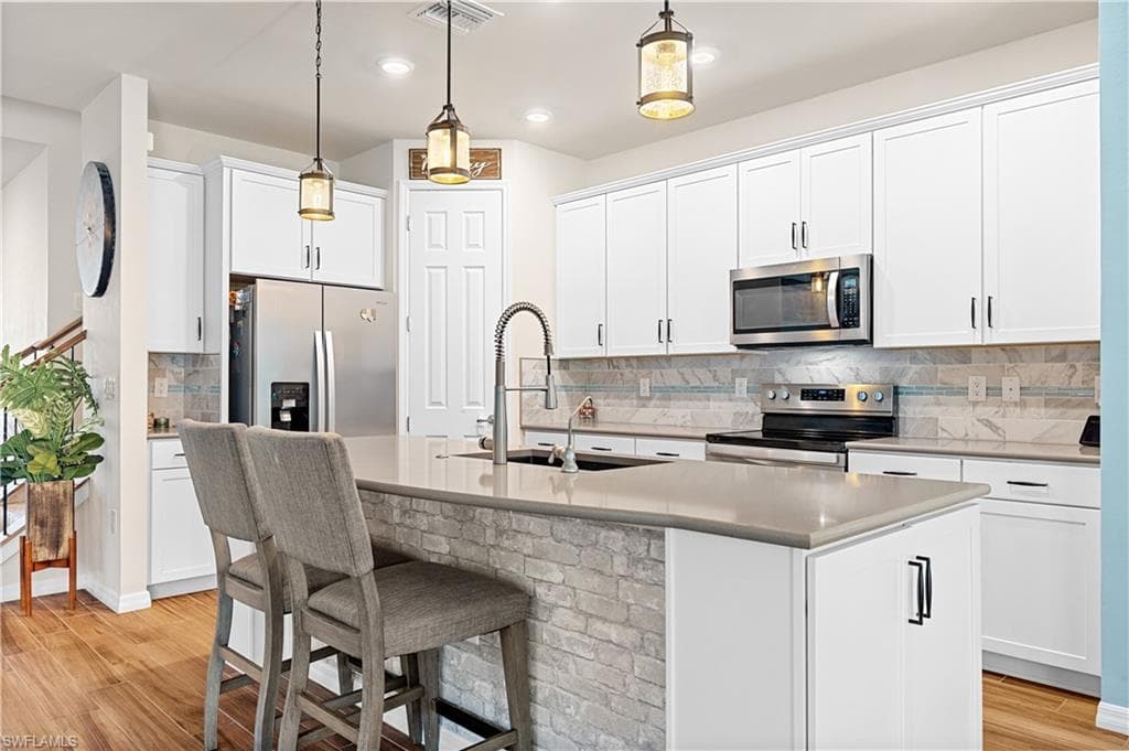 Kitchen featuring backsplash, light wood-style floors, stainless steel appliances, a kitchen breakfast bar, and recessed lighting