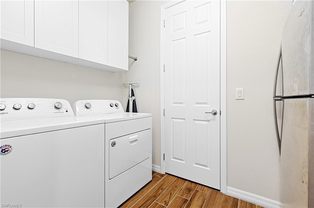 Washroom featuring wood tiled floors, separate washer and dryer, and cabinet space