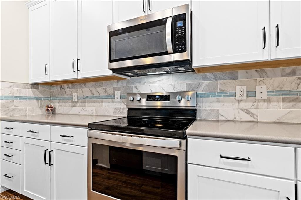 Kitchen with appliances with stainless steel finishes, white cabinets, light countertops, and tasteful backsplash