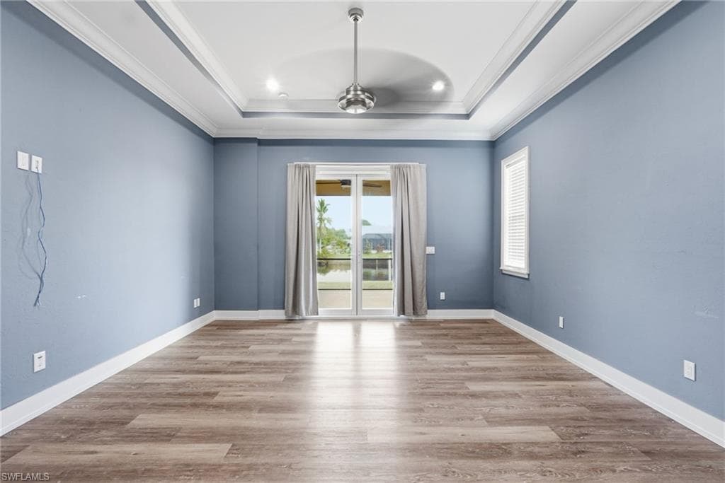 Empty room featuring light wood finished floors, crown molding, a ceiling fan, a raised ceiling, and recessed lighting