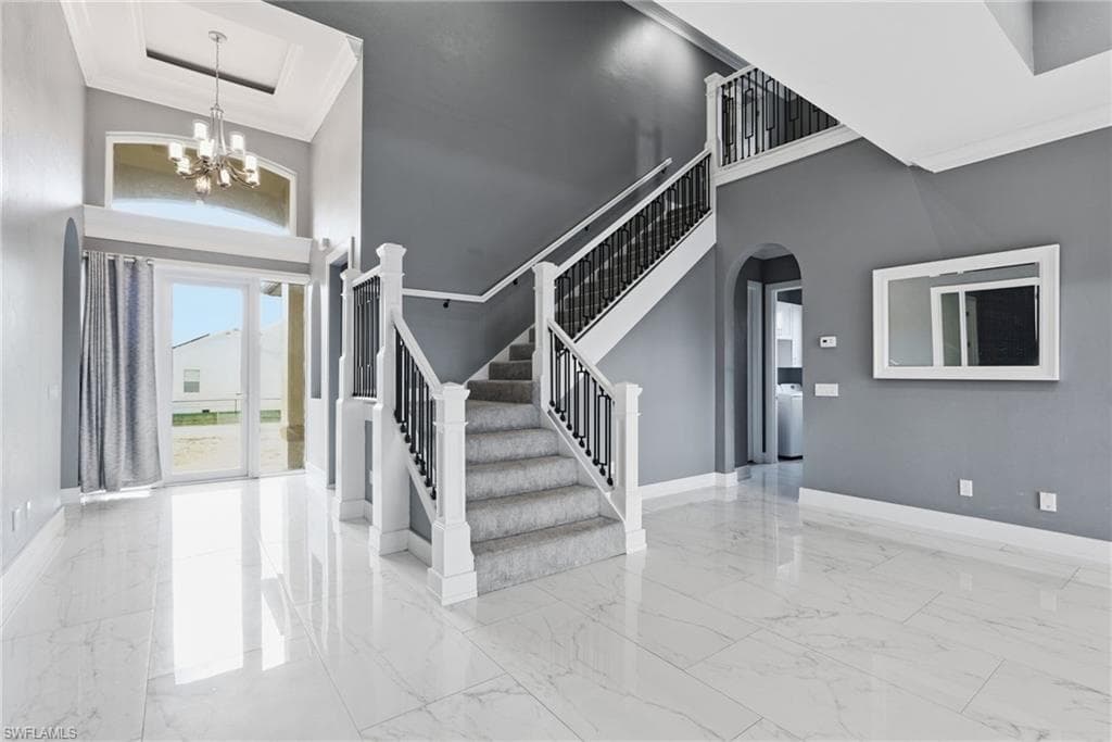 Entrance foyer with crown molding, a high ceiling, arched walkways, stairway, and a chandelier