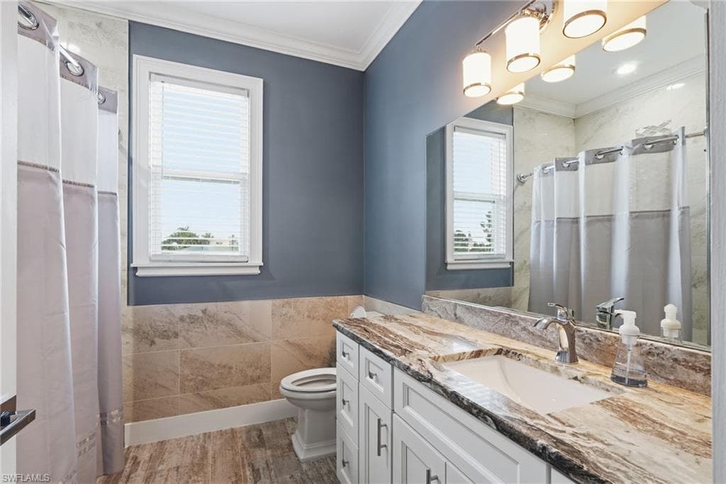 Bathroom featuring crown molding, vanity, a shower with shower curtain, wainscoting, and tile walls