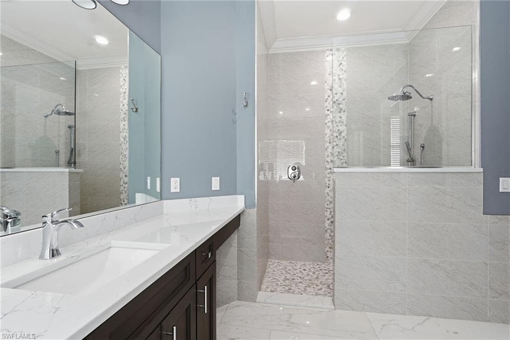 Bathroom featuring a walk in shower, vanity, light marble finish floors, crown molding, and recessed lighting