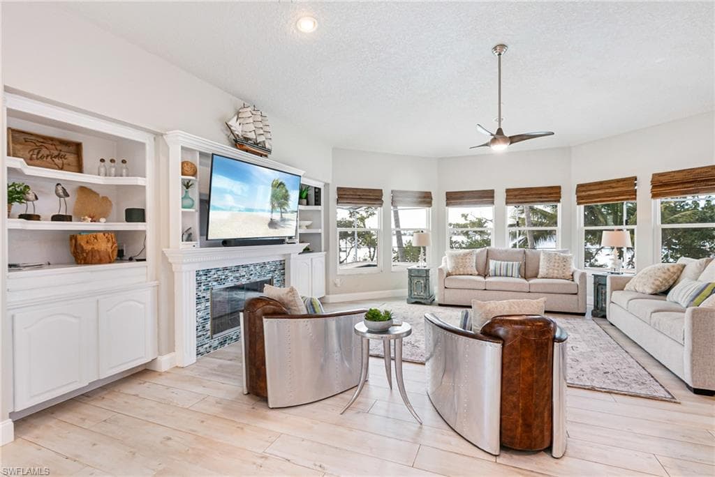 Living area featuring a textured ceiling, a ceiling fan, a tile fireplace, light wood finished floors, and built in shelves