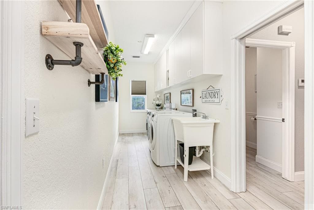 Laundry area featuring light wood finished floors, cabinet space, and washer and dryer