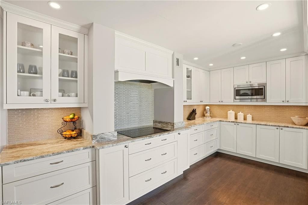 Kitchen featuring white cabinets, light stone countertops, recessed lighting, glass insert cabinets, and tasteful backsplash