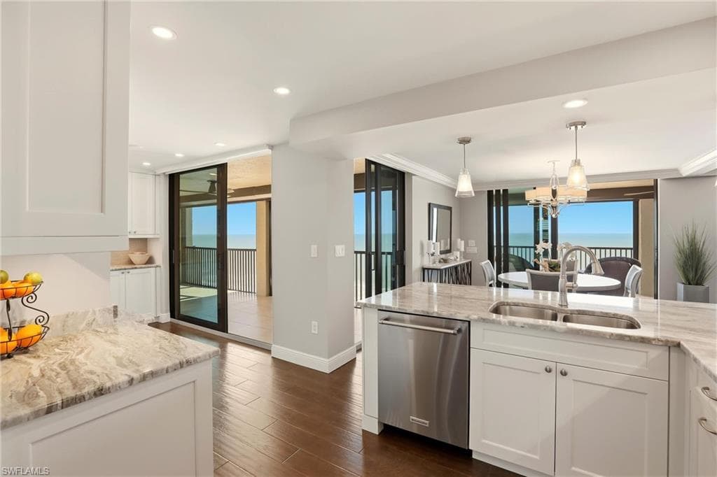 Kitchen featuring white cabinets, light stone countertops, stainless steel dishwasher, dark wood finished floors, and healthy amount of natural light