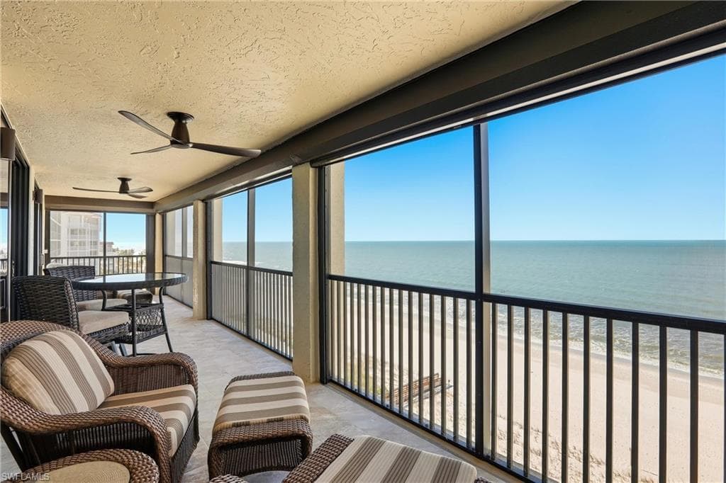 Sunroom featuring a balcony, ceiling fan, and view of water and beach
