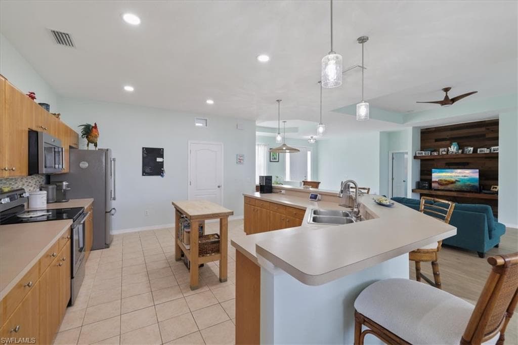 Kitchen featuring a kitchen breakfast bar, appliances with stainless steel finishes, a spacious island, light countertops, and hanging light fixtures