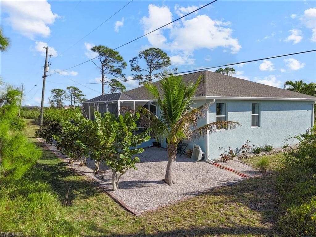 Rear view of house featuring a lanai, stucco siding, roof with shingles, and a yard