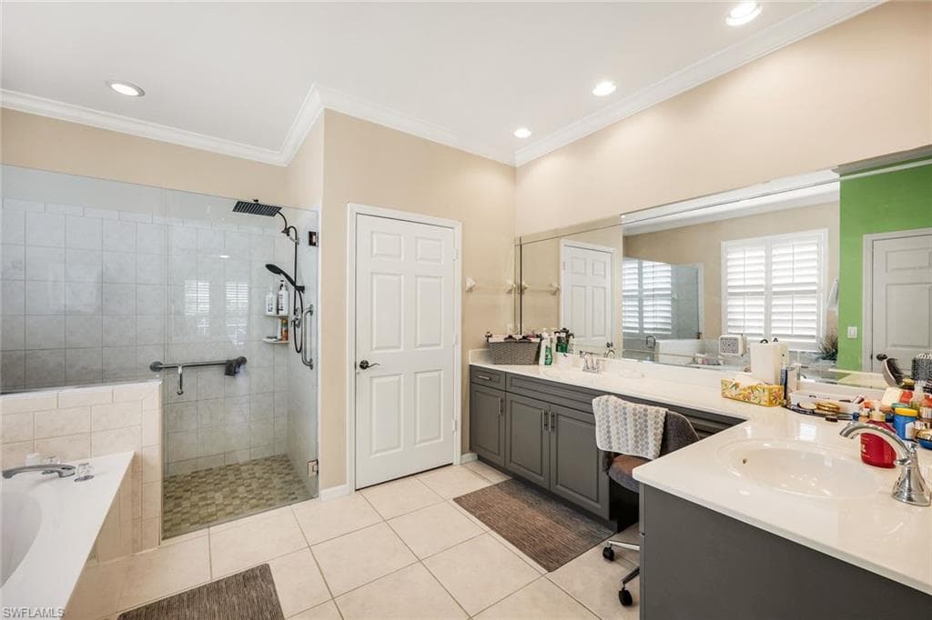 Bathroom featuring a shower stall, a garden tub, double vanity, light tile patterned floors, and ornamental molding