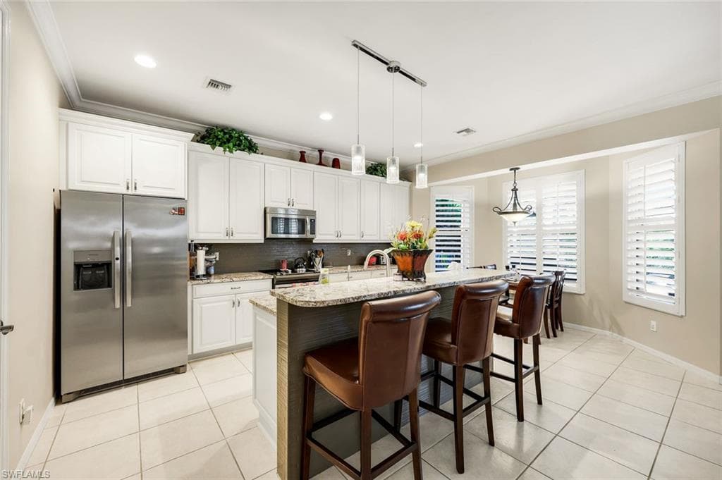 Kitchen with appliances with stainless steel finishes, light stone counters, white cabinets, crown molding, and hanging light fixtures