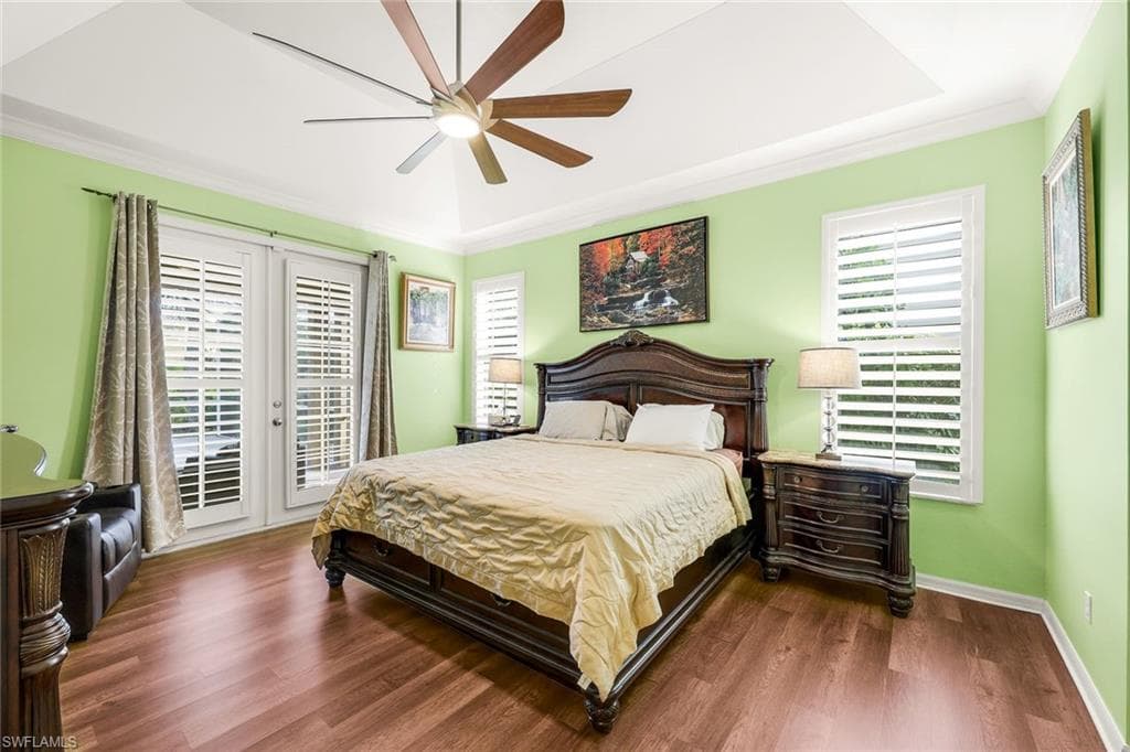 Bedroom with access to outside, wood finished floors, a ceiling fan, ornamental molding, and a raised ceiling