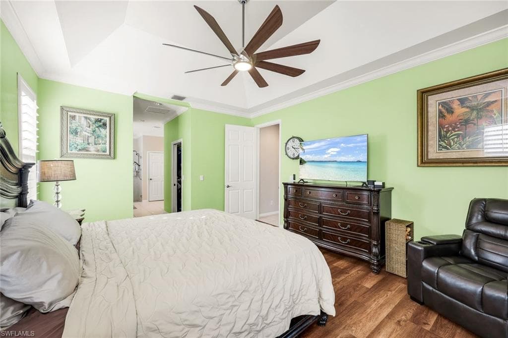 Bedroom with a tray ceiling, ornamental molding, dark wood-type flooring, and ceiling fan