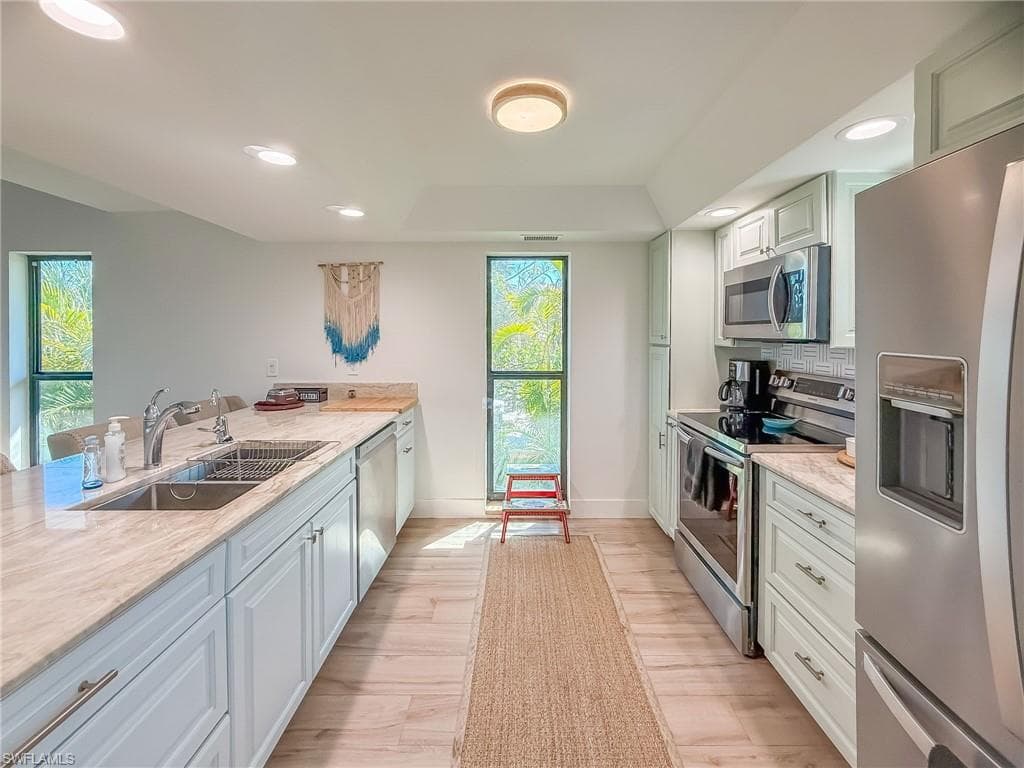 Kitchen with sink, backsplash, light stone counters, stainless steel appliances, and light hardwood / wood-style flooring