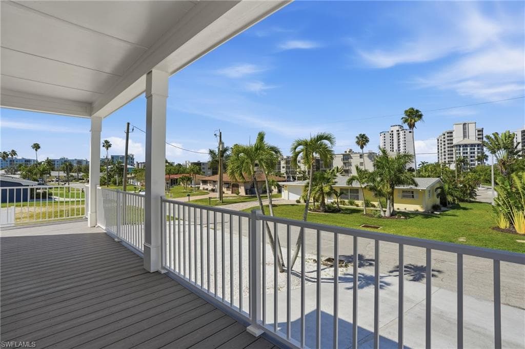 Elevated balcony with wood-finish flooring, white railing, and decorative columns - Virtually Edited Image