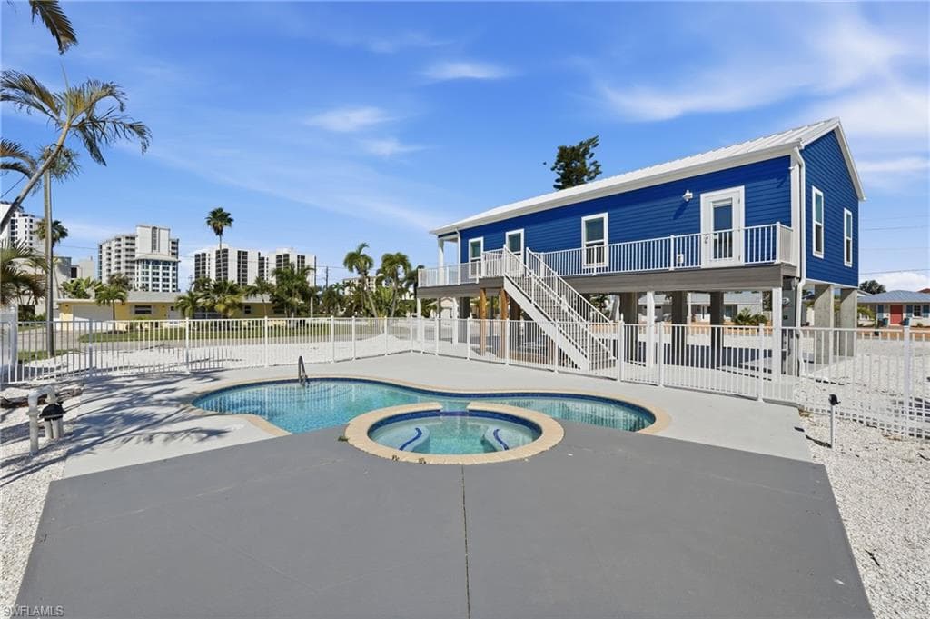 Elevated coastal property featuring a blue exterior with white trim, a multi-tiered pool and spa, and a surrounding privacy fence - Virtually Edited Image