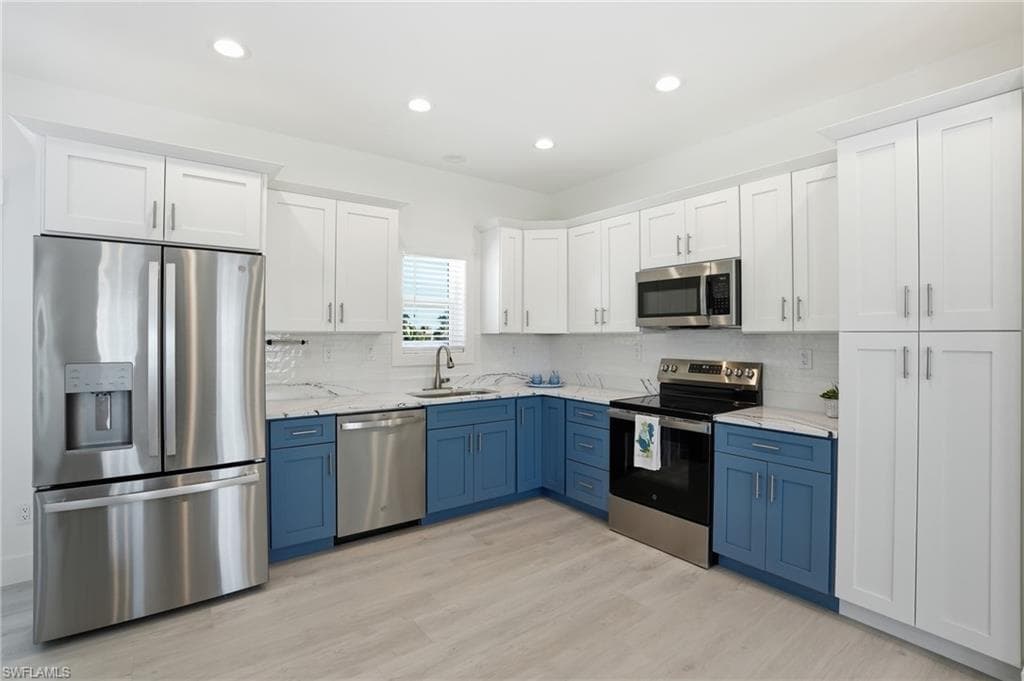 Contemporary kitchen featuring two-tone cabinetry, stainless steel appliances, marble-look countertops, a geometric tile backsplash, and light wood-finish flooring - Virtually Edited Image