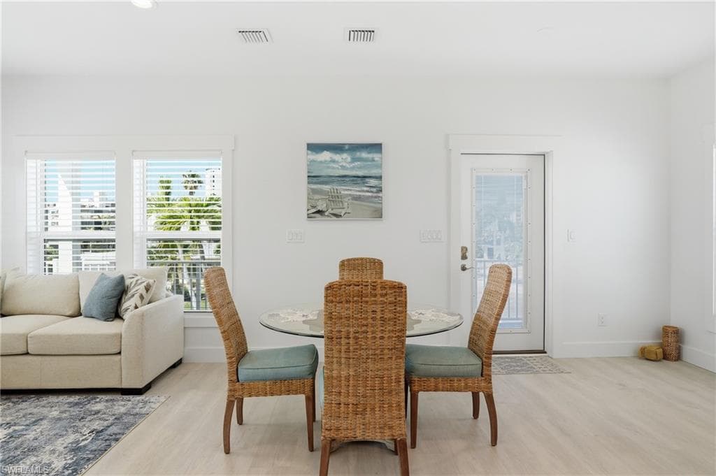 Open-concept living area with light wood-finish flooring, white walls, and recessed lighting - Virtually Edited Image
