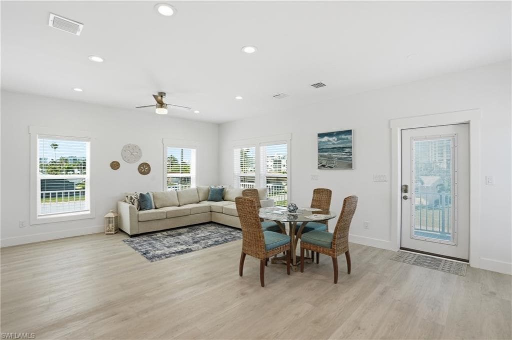 Expansive living area featuring light wood-finish flooring, white walls, and recessed lighting - Virtually Edited Image