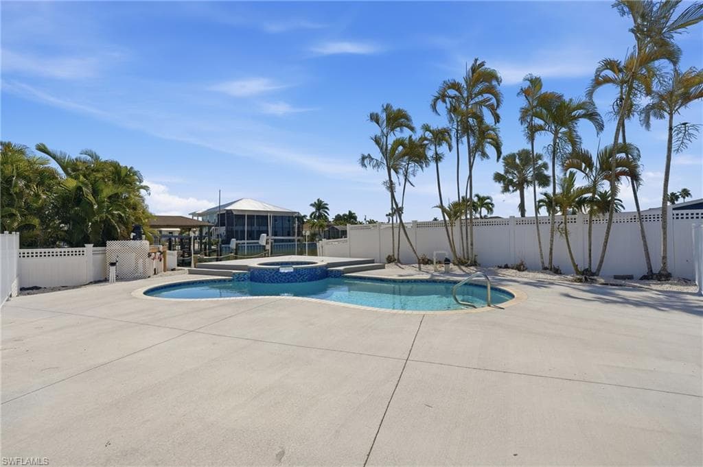 Curved swimming pool with an integrated spa, surrounded by expansive concrete decking - Virtually Edited Image