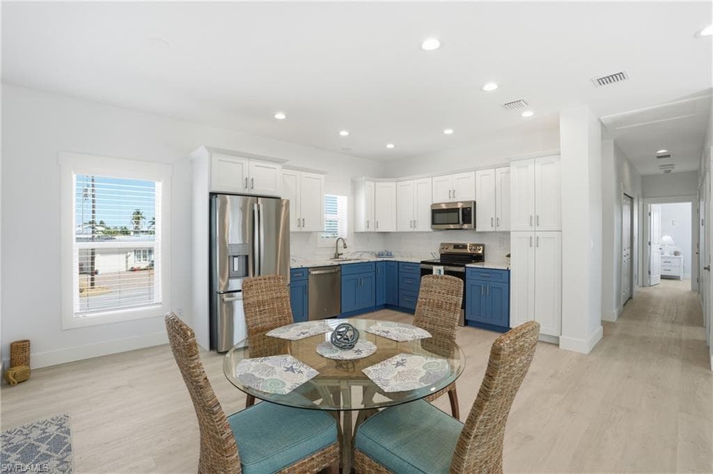 Open-concept kitchen and dining area featuring two-tone cabinetry, stainless steel appliances, recessed lighting, and wood-finish flooring - Virtually Edited Image