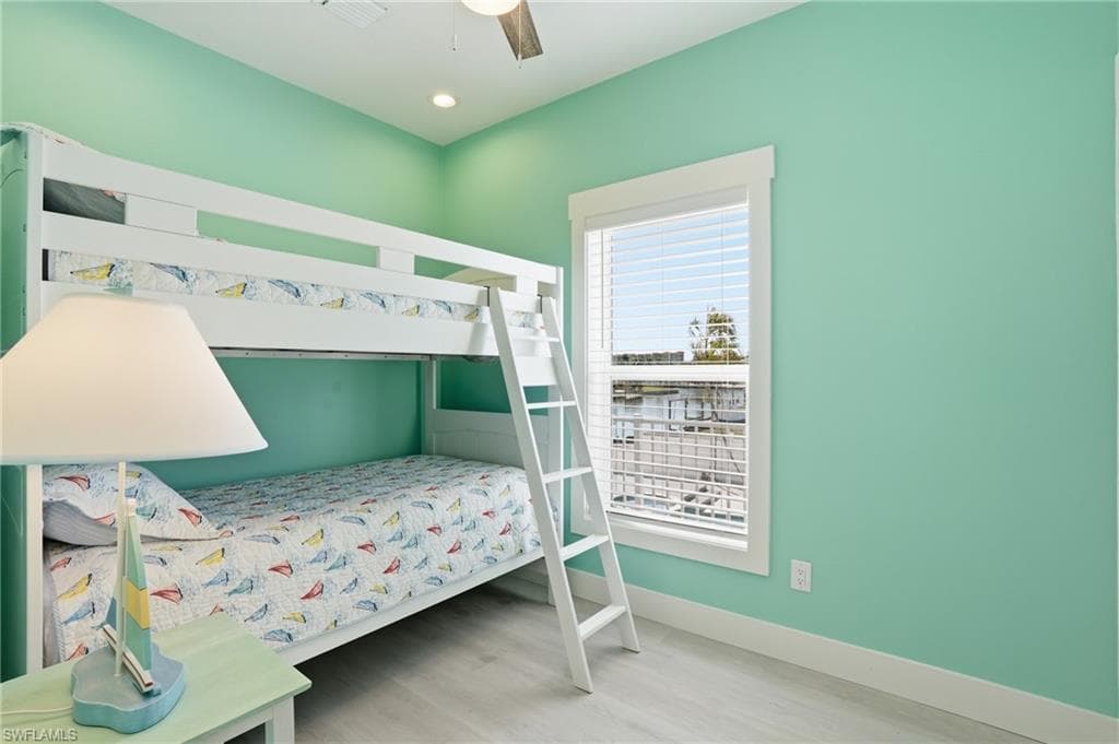 This room features a white bunk bed with a ladder, light green walls, and wood-finish flooring - Virtually Edited Image
