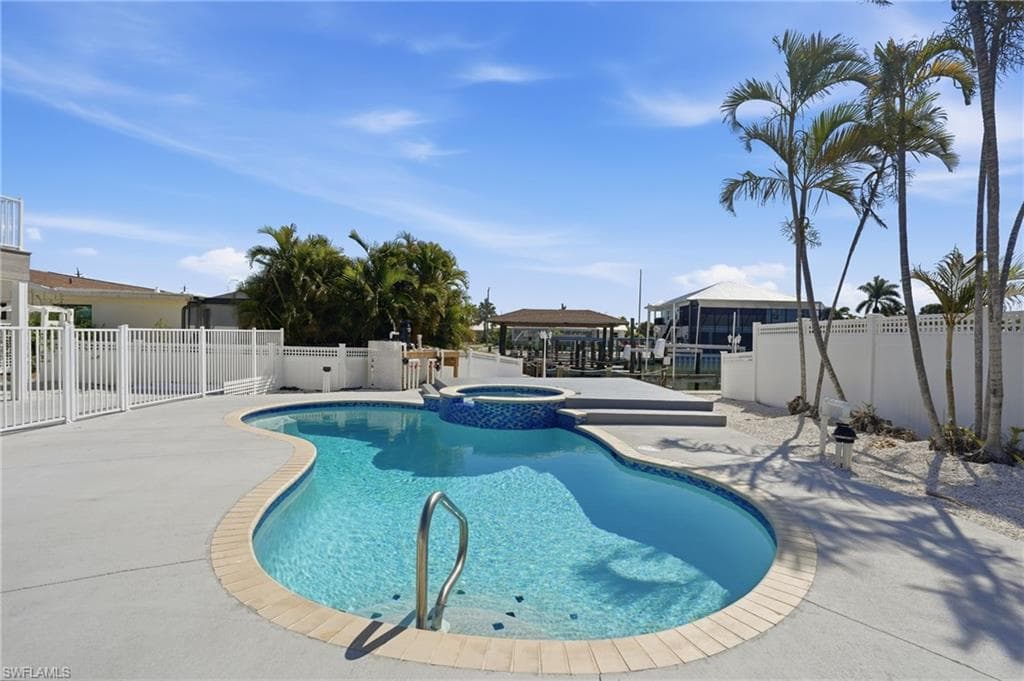 Resort-style pool area featuring a freeform swimming pool with integrated spa, surrounding concrete patio, and white privacy fencing - Virtually Edited Image