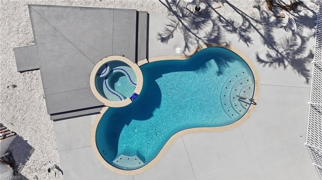 Kidney-shaped swimming pool featuring an integrated spa with blue tile accents - Virtually Edited Image