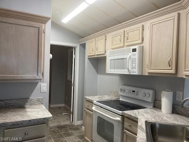 Kitchen with white appliances, light brown cabinetry, light countertops, and vaulted ceiling