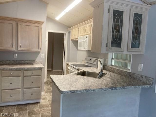 Kitchen with white appliances, vaulted ceiling, light countertops, glass insert cabinets, and a peninsula