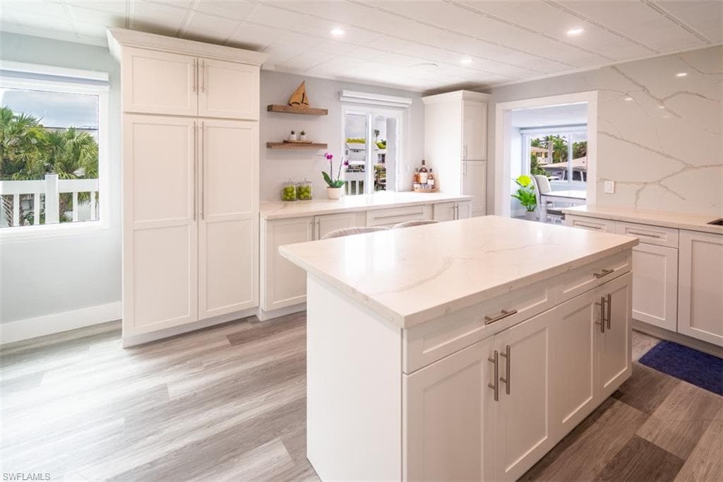 Kitchen featuring white cabinets, light stone countertops, a center island, open shelves, and light wood-type flooring