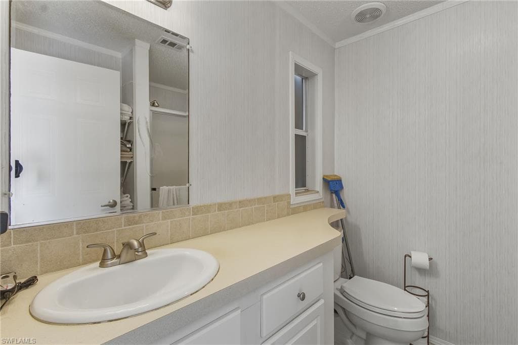 Bathroom featuring vanity, a shower stall, ornamental molding, tasteful backsplash, and wallpapered walls